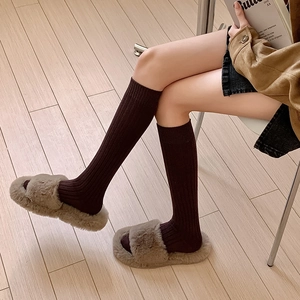 Detailed knit texture of dark brown ribbed knee-high socks with fuzzy grey home slippers
