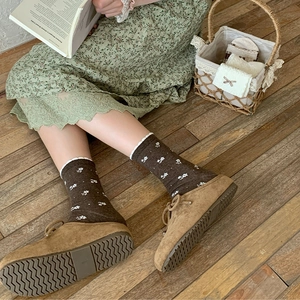 Detailed close-up of dark brown floral crew socks with ruffle edges and suede lace-up shoes