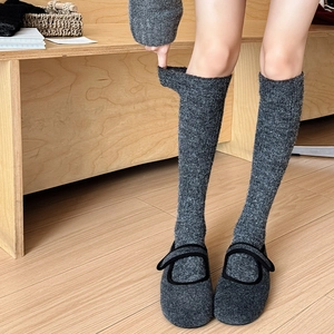 Thick grey knitted calf socks paired with felt Mary Jane shoes on wood floor