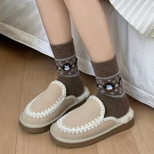 Close-up of beige suede mules with fuzzy lining and brown knit socks on wooden floor