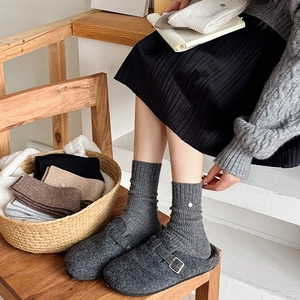 Detail view of thick grey wool socks with button accents and cozy felt mule slippers