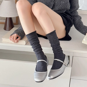 Detail of dark grey slouch socks paired with silver Mary Janes in a stylish home setting