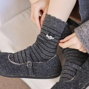 Détail de chaussettes en laine à rayures grises avec broderie ours et bord volanté