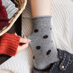 Detail of grey knitted mid-calf wool socks with black polka dots on a cozy blanket
