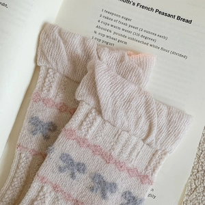 Close-up of wool socks featuring knit cable textures and pink bow jacquard patterns