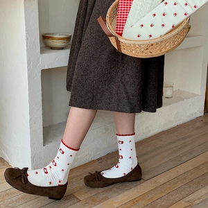 Detail of white mid-calf socks with red floral print and bear patterns on white wall