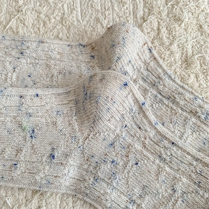 Macro shot of cream wool socks featuring colorful flecks and thick diamond knit texture