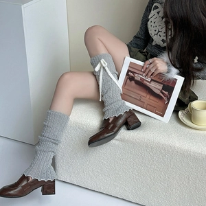 Gray knitted leg warmers with white ribbons paired with brown loafers on model