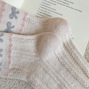 Close-up of knit wool socks with pink wavy edges, bow details, and hollow textures