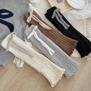 Close-up of knit leg warmers with bow ties and ruffle edges in four soft colors