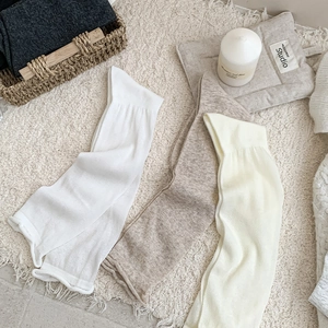 Close-up of knit leg warmers in neutral tones with ribbed texture on soft rug