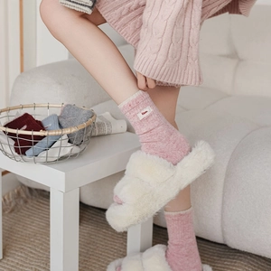 Gros plan de chaussettes en maille rose avec broderie 'Nice' et pantoufles en peluche