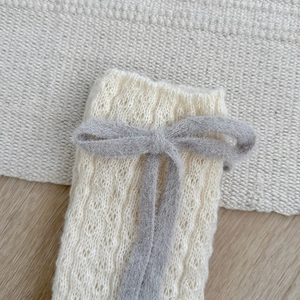 Close-up of knit leg warmer with gray plush bow and hollow crochet texture detail