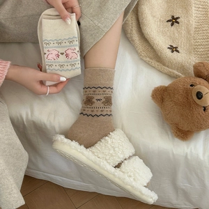 Detail of plush bear pattern socks paired with cozy white fleece slippers on a bed