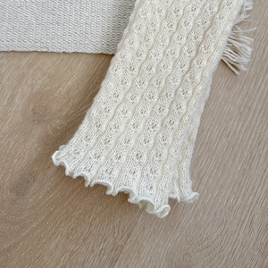 Close-up of white knitted leg warmers with hollow crochet texture and ruffled edges