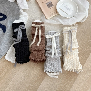 Close-up of four-color knitted leg warmers with ribbon bows and wavy scalloped edges