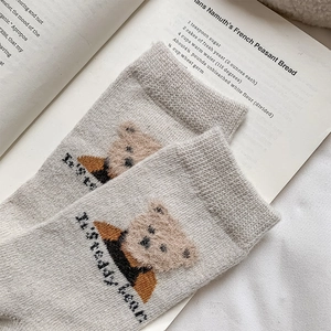 Close-up of a light grey knitted sock featuring a brown flocked teddy bear pattern