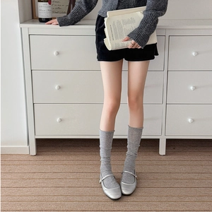 Close-up of grey knitted slouch socks styled with silver Mary Jane shoes and black shorts