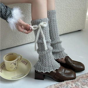 Detail of grey ribbed knit leg warmers with white plush bows and ruffled hem edges