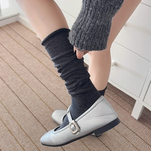 Close-up of dark grey slouch socks paired with silver metallic Mary Jane shoes on a rug