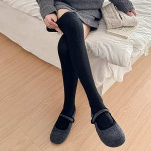 Close-up of black over-the-knee knit socks paired with grey felt buckle shoes on wood floor