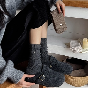Close-up of wool socks with decorative shell buttons and cozy felt clogs in a home setting