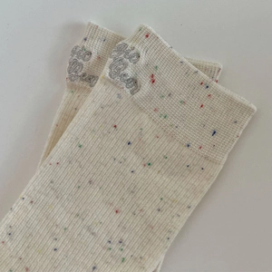 Détail de chaussettes en maille mouchetée avec broderie Bonjour et côtes verticales