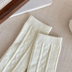 Detail of cream knit knee socks featuring classic diamond texture and ribbed cuff design