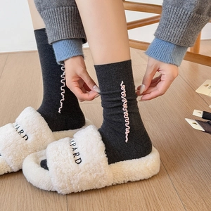 Detail of grey wool socks with pink wavy embroidery and white fuzzy slippers on wood