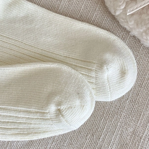 Close-up of off-white ribbed knit socks with detailed texture on linen background