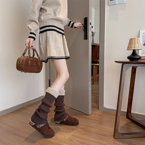 Gros plan sur jambières en tricot marron avec sabots en daim et jupe plissée beige assortie