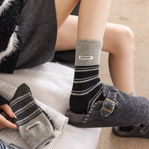 Detail of gray striped knit socks with brand label and wool felt clogs in a cozy setting