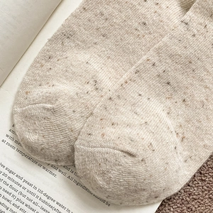 Détail macro de chaussettes en laine mouchetée beige montrant la texture du tricot