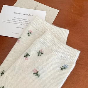 Close-up of floral wool socks with pink and blue knit patterns on soft cream fabric