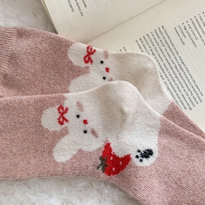 Close-up of cute pink knitted socks with rabbit and strawberry embroidery on faux fur