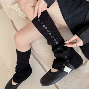 Close-up of black ribbed leg warmers featuring vertical decorative buttons and knit texture