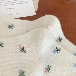Close-up of white wool socks with delicate pink and blue floral embroidery texture