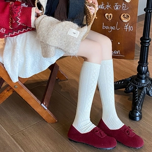 Detail of white knit knee-high socks featuring argyle patterns and ribbed texture for women
