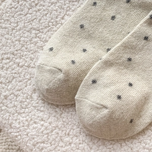 Detailed texture of oatmeal wool knit socks with dark gray polka dots and soft wool background