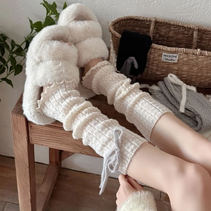 Dettaglio di scaldamuscoli in maglia con fiocchi di peluche grigi e bordi a volant su ciabatte