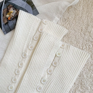 Detailed close-up of white ribbed knit leg warmers with elegant decorative side buttons