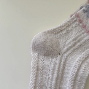 Detail von weißen Wollsocken mit Zopfmuster und buntem Fair-Isle-Strickmuster für Damen