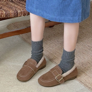 Brown fleece-lined loafers with metal buckle worn with thick knit socks for winter comfort
