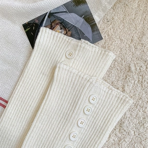 Detail of cream rib-knitted leg warmers with side button accents and cozy texture