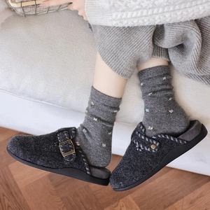 Close-up of dark grey felt clogs with bronze buckle and thick sole on a wooden floor
