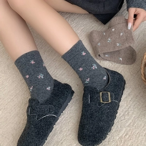 Floral knit wool socks paired with grey felt clogs on a plush rug for winter