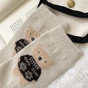 Close-up of oatmeal wool socks with cartoon teddy bear jacquard pattern on a cozy rug