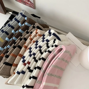 Detail view of multi-color striped ribbed cotton socks neatly stacked on a minimal white desk