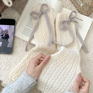 Dettaglio di scaldamuscoli in maglia crema con fiocco grigio e bordi a balze smerlati
