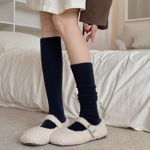 Detail of warm off-white plush Mary Jane shoes paired with thick black ribbed knit socks